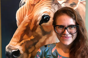 Serrin stands in front of a picture of a cow